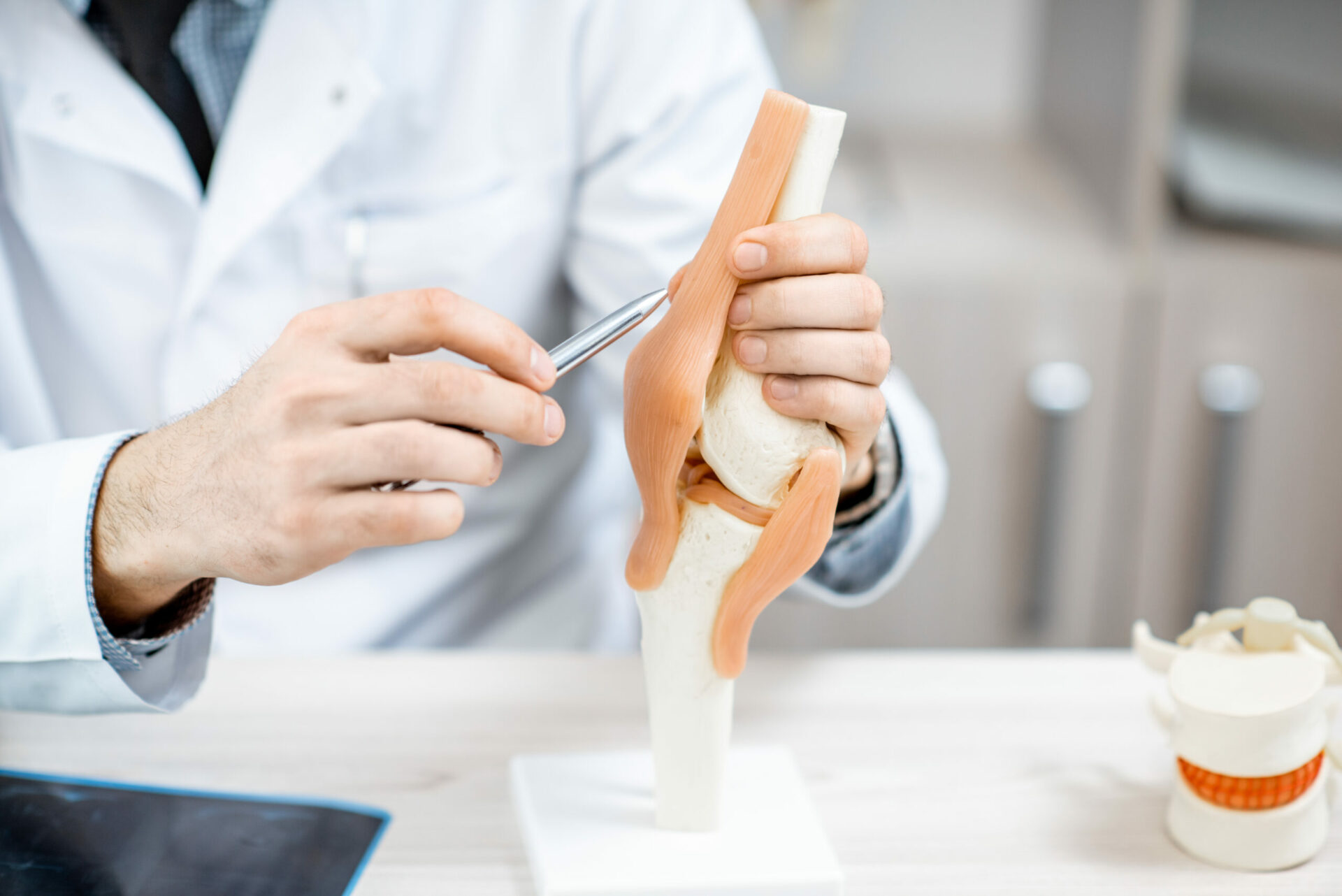 Close-up of the therapist showing knee joint model during the medical consultation